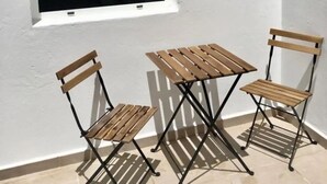 A small outdoor seating area with two wooden chairs and a table against a white wall, adjacent to a window. - Apartamento Norte (Arrecife)