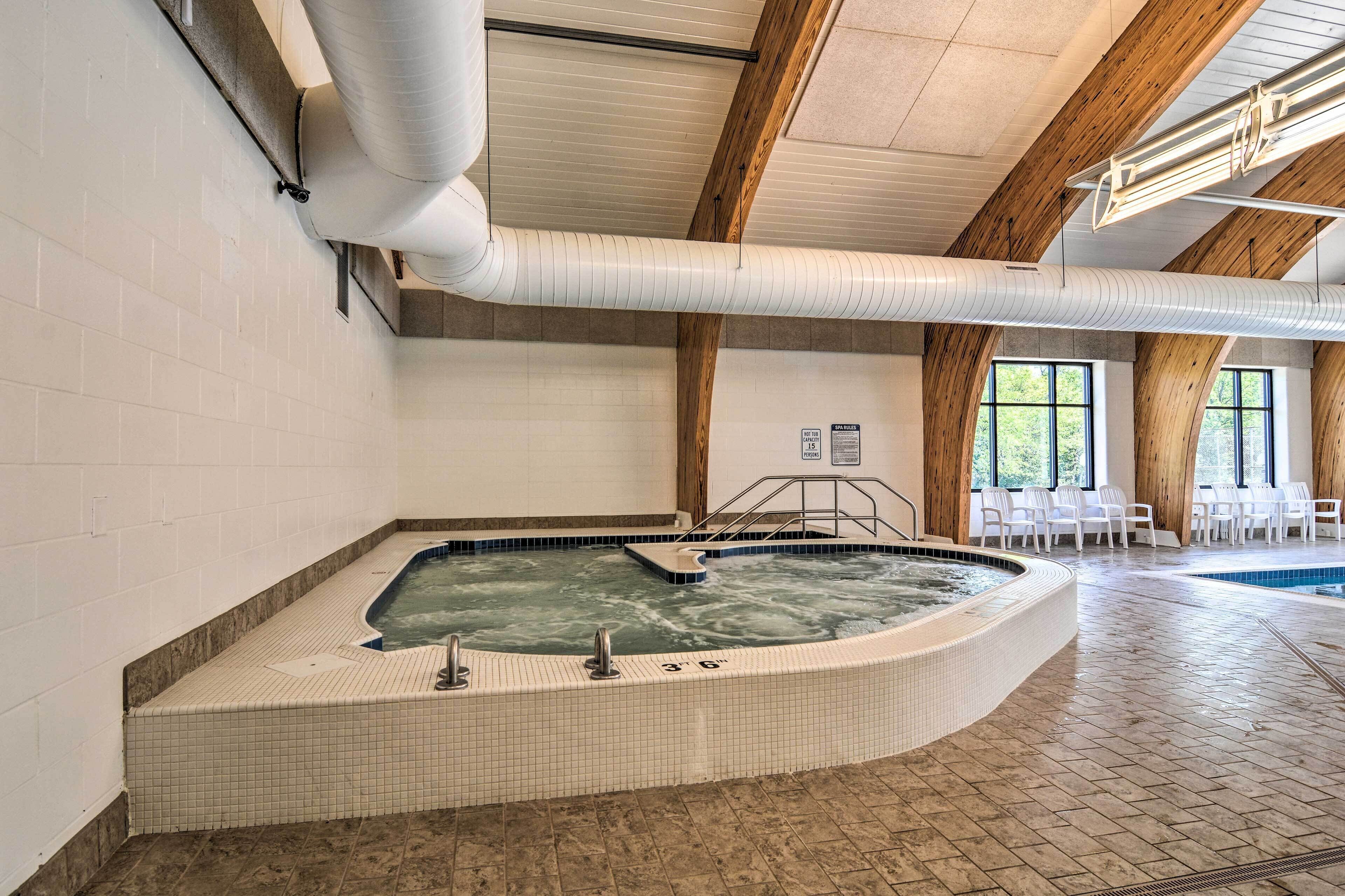 A hot tub in a room with tiled walls, wooden beams, and a pool.