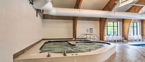 A hot tub in a room with tiled walls, wooden beams, and a pool.