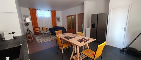 Un espacio habitable pequeño con comedor, sofá, refrigerador y aspiradora.