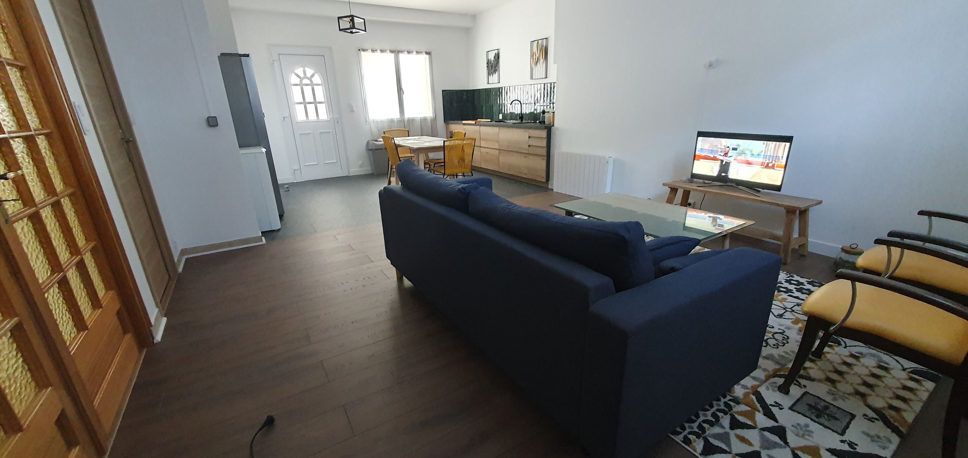 En stue med sofa, fjernsyn og spiseplads med stole og bord.