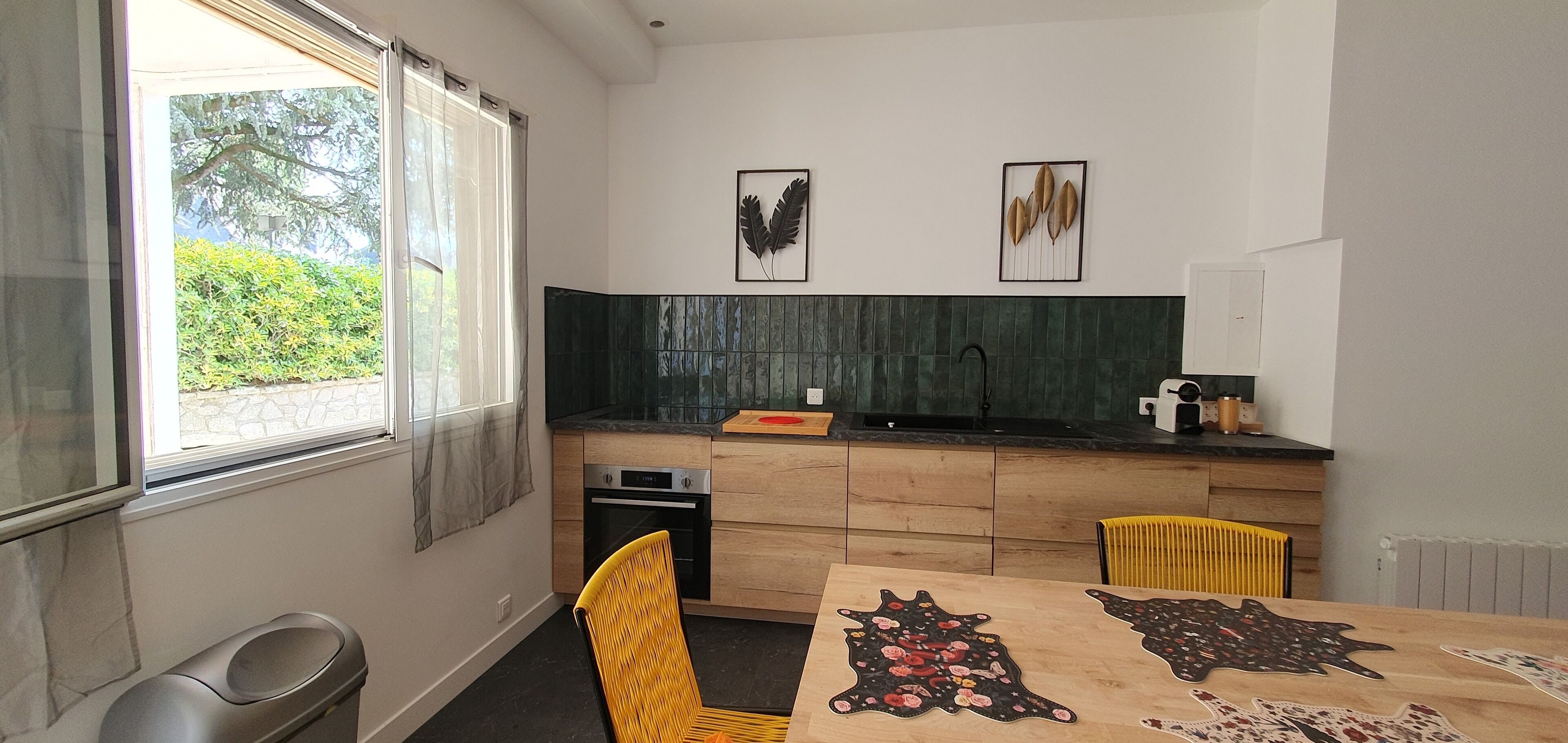 A modern kitchen with a large window, a sink, and a dining table with a unique rug.