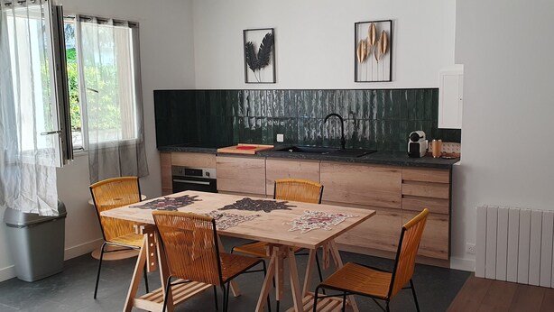 Uma cozinha moderna com uma mesa e cadeiras de madeira, bancada preta e painel de fundo verde.