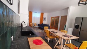 Uma sala de estar moderna com sofá, mesa de jantar, cadeiras e uma cozinha com geladeira.