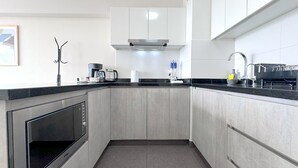A modern kitchen with grey cabinets, a built-in oven, a coffee maker, and a sink with a dish rack. - Ocean View 1BR - TV 65" - Pool - Jacuzzi 1609 (Barranco)