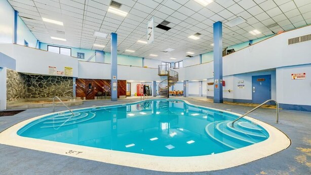 An indoor swimming pool with a stone wall, a spiral staircase, and a blue ceiling.