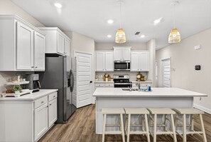 Una cocina moderna con muebles blancos, electrodomésticos de acero inoxidable y una isla central con taburetes de bar.