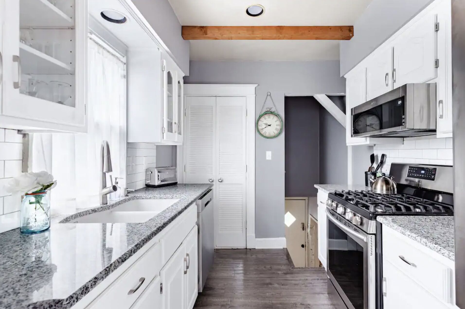 Una cocina moderna con gabinetes blancos, encimeras de granito y electrodomésticos de acero inoxidable, incluyendo una estufa y un microondas.