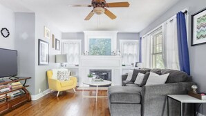 Una sala de estar con chimenea, un sillón amarillo, un sofá gris y un televisor.