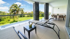 A balcony with a view of a green landscape and palm trees, furnished with a table and chairs. - Sirenita G. Infinity pool - At Mareazul (Playa del Carmen)