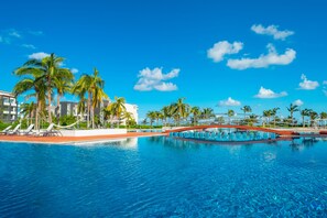 Una piscina con sillones de descanso y palmeras, rodeada de edificios modernos.