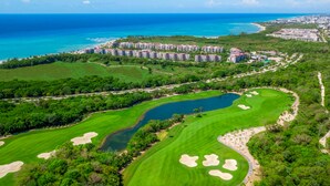 A golf course with a lake, surrounded by greenery and a coastal view. - Sirenita G. Infinity pool - At Mareazul (Playa del Carmen)