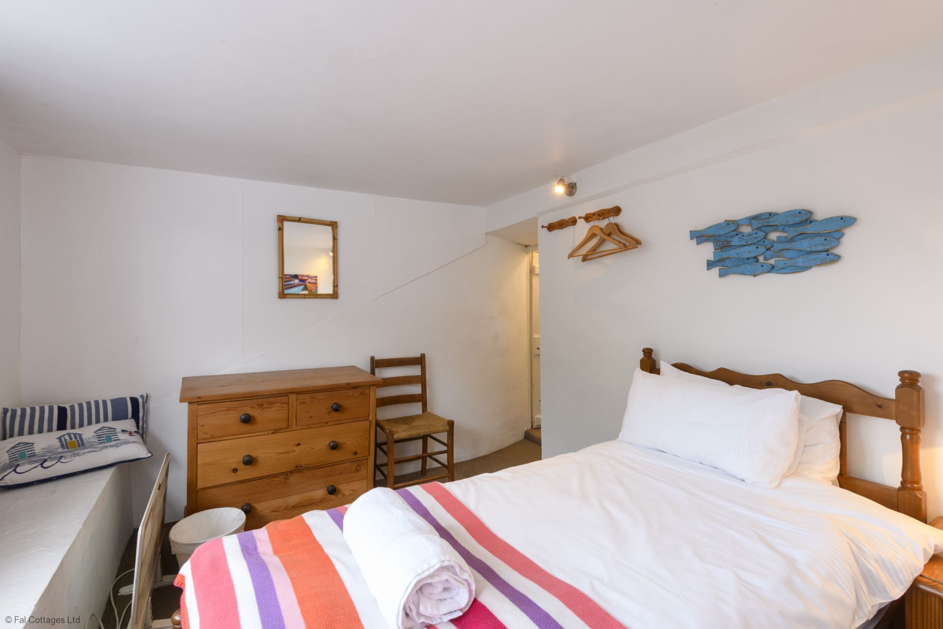 Une chambre à coucher comprenant un lit, une commode en bois, une chaise, un miroir et des œuvres d’art murales.