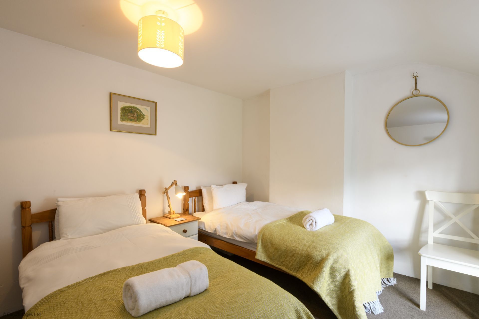 A hotel room with two beds, a nightstand with a lamp, a framed picture on the wall, and a round mirror.