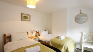 A hotel room with two beds, a nightstand with a lamp, a framed picture on the wall, and a round mirror.
