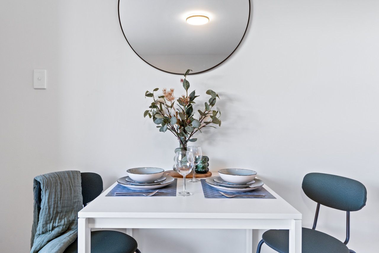 A dining table with two chairs, a vase with flowers, and a wall-mounted light fixture.