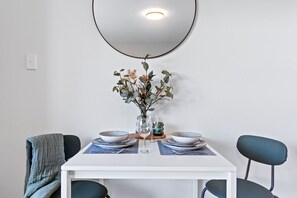 A dining table with two chairs, a vase with flowers, and a wall-mounted light fixture. - Cul-de-Sac Charm St Kilda (St Kilda)