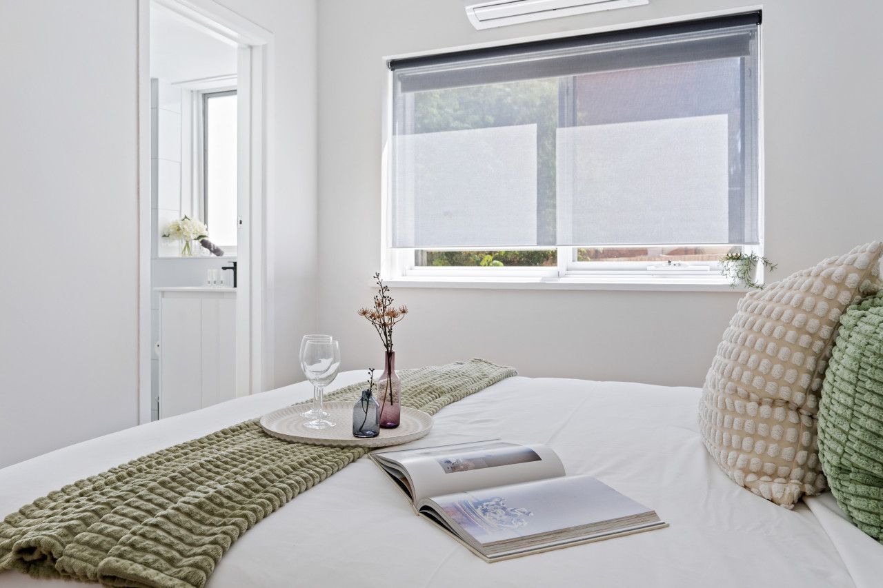 A neatly made bed with a magazine, a glass of water, and a vase with flowers.