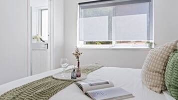 A neatly made bed with a magazine, a glass of water, and a vase with flowers.