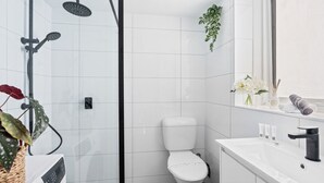 Une salle de bain moderne avec une douche à parois de verre, des toilettes, un lavabo avec un miroir et une étagère contenant des articles de toilette.