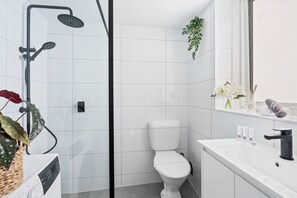 Ein modernes Badezimmer mit einer Duschkabine, einer Toilette, einem Waschbecken mit Spiegel und einem Ablagefach für Toilettenartikel.