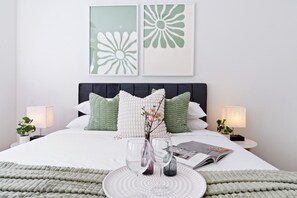 A neatly made bed with a white and green color scheme, two bedside lamps, and a magazine on the bed.