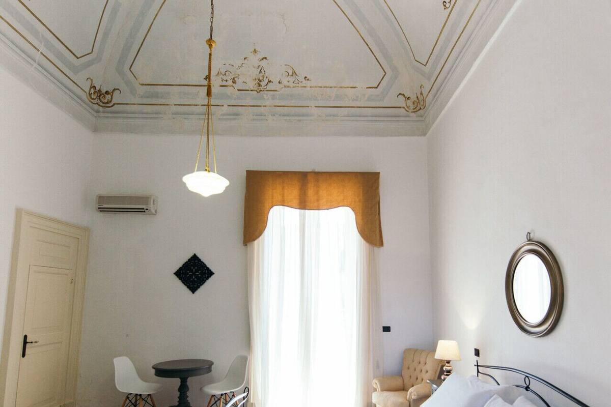 Una habitación de hotel con cama, mesita de noche, silla y una pequeña mesa con lámpara.