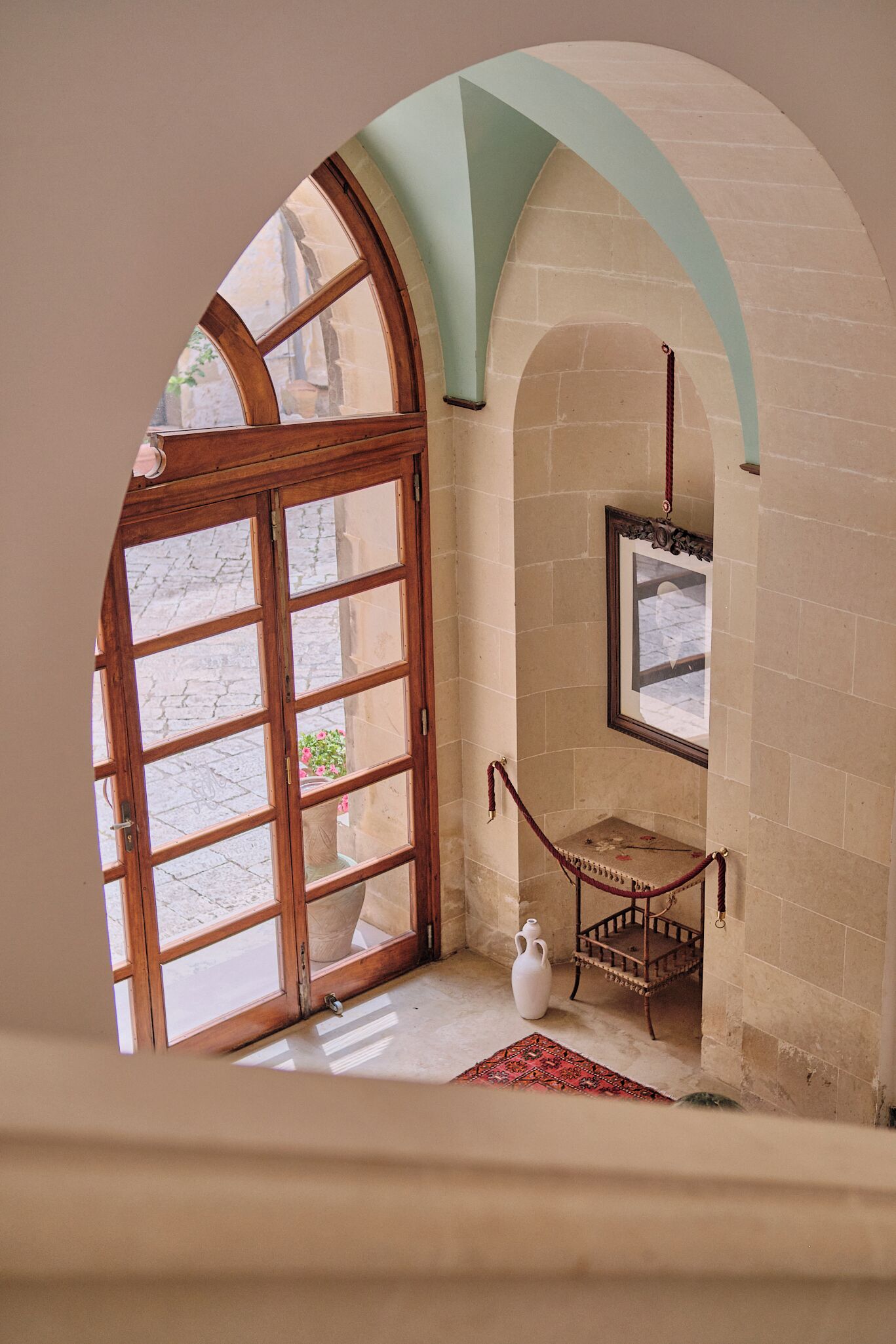 An arched doorway leading to a room with a stone fireplace, a white vase, and a red rug.