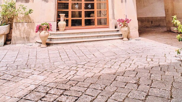 Un edificio histórico con una amplia entrada en arco, paredes de piedra y plantas en macetas.