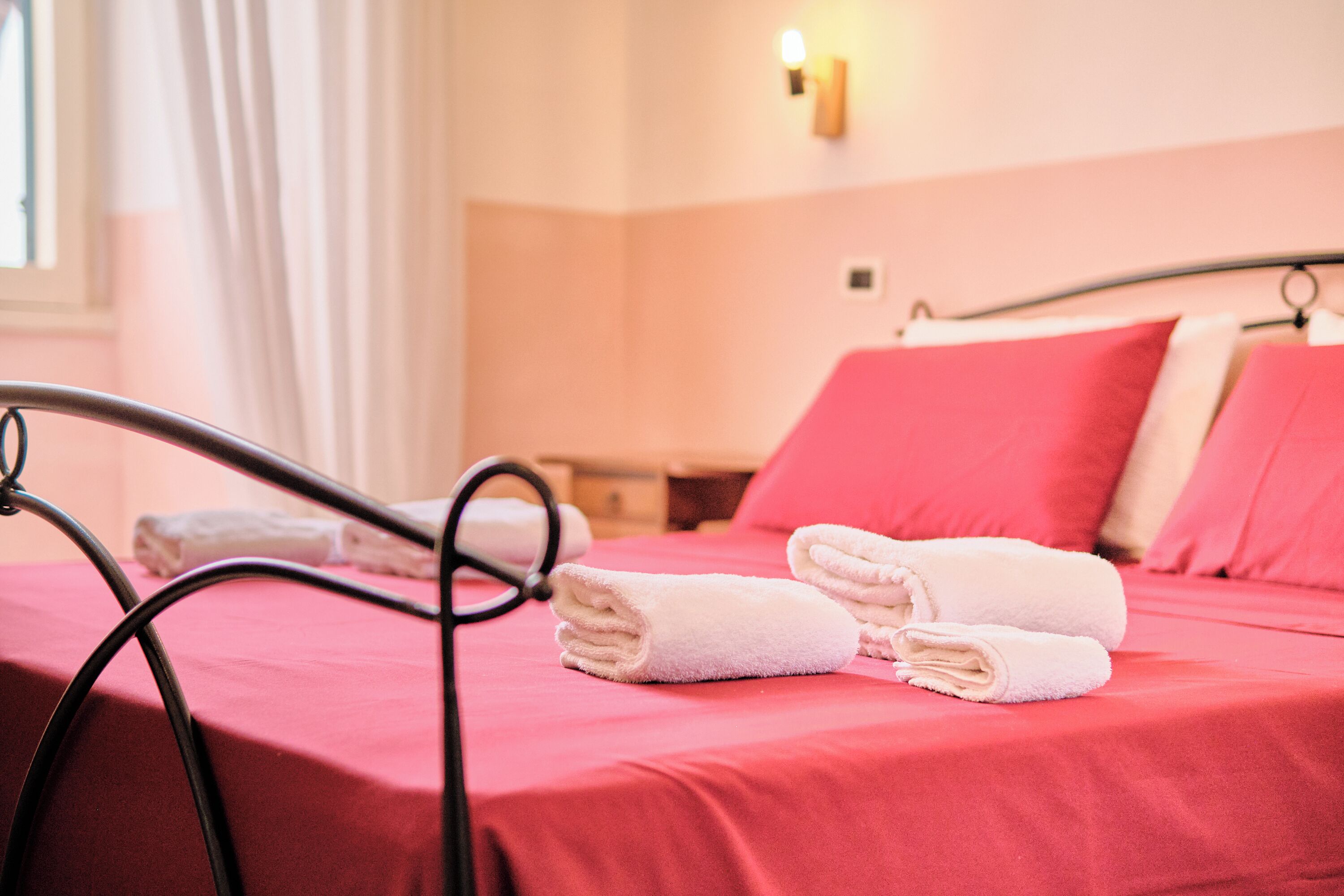 Ein ordentlich bezogenes Bett mit rosa Bettwäsche und weißen Handtüchern, ein Metallbettgestell und eine Wandleuchte.