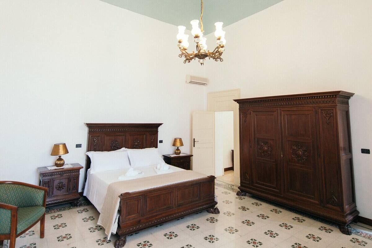 Un dormitorio con una cama grande, un armario de madera, una araña y baldosas de suelo estampadas.