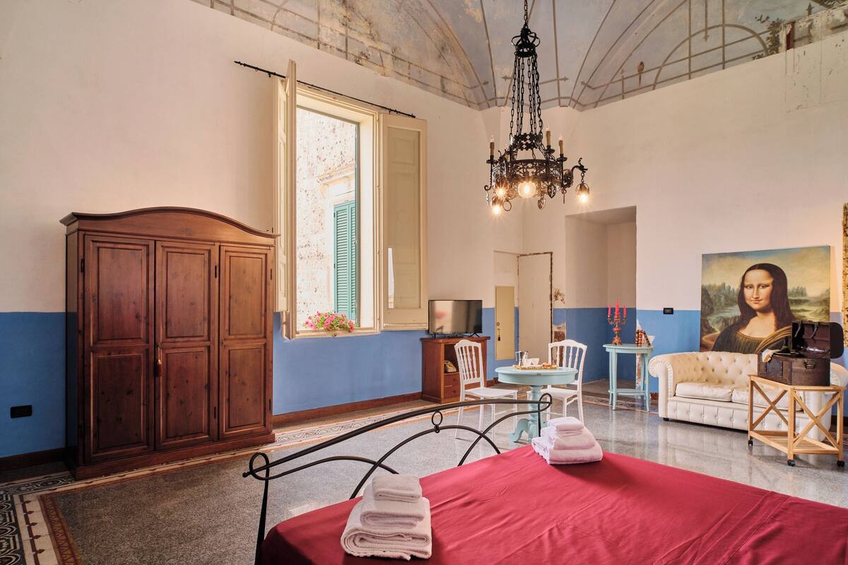 Habitación de hotel con una cama, un armario de madera, una araña, un televisor y un cuadro de la Mona Lisa.