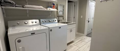 Een wasserette met twee Maytag wasmachines en drogers, een aanrecht met een spoelbak en een spiegel boven de spoelbak.