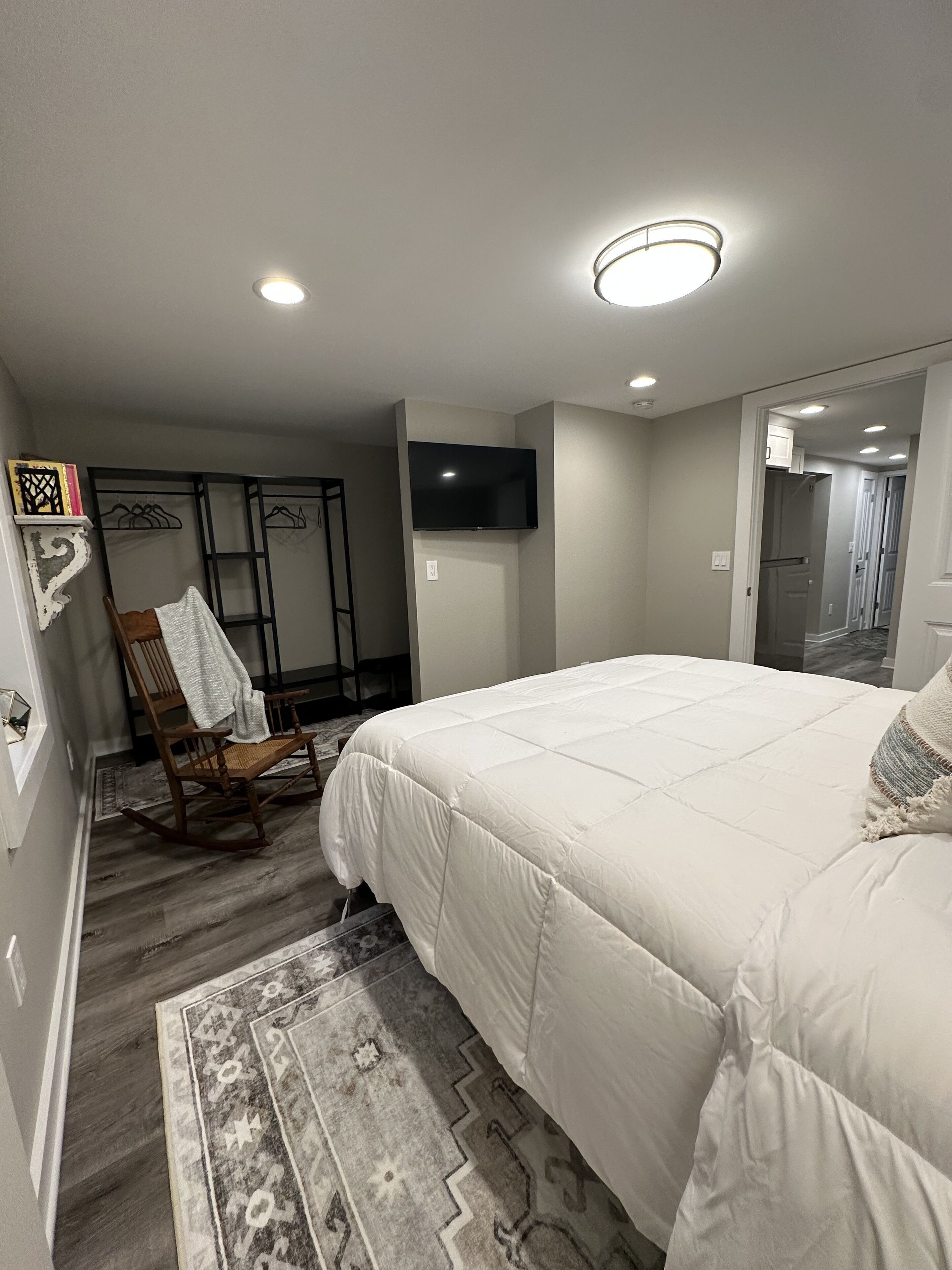A bedroom with a large bed, a television mounted on the wall, and a chair with a towel.