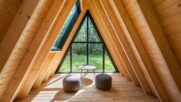 A triangular attic room with wooden beams, a large window, and two round ottomans.