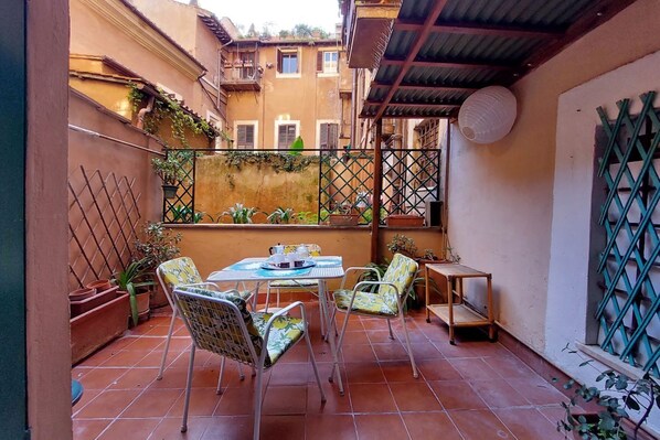 A patio with a table and chairs, surrounded by potted plants and a metal fence.