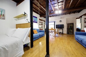 A room with a bed, a blue sofa, a wooden floor, a TV, and a mirror.