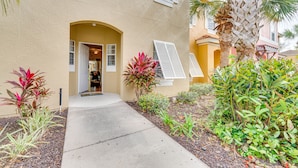 A building with a beige exterior, a concrete pathway leading to an entrance with a door, and various plants around. - 4 Mi to Disney: Emerald Island Resort Home! (Kissimmee)