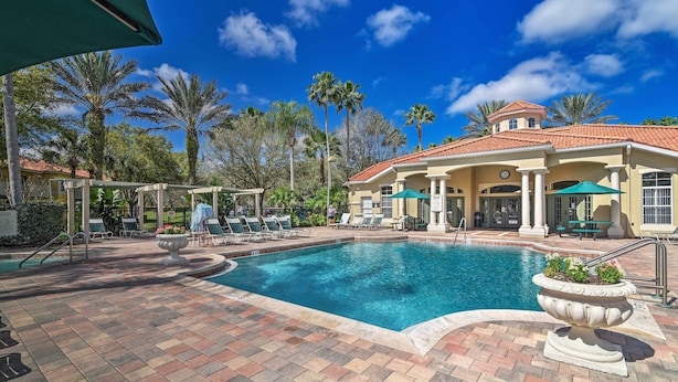 A swimming pool area with lounge chairs, a covered seating area, and a building with a tiled roof. - 4 Mi to Disney: Emerald Island Resort Home! (Kissimmee)