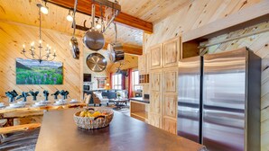 A modern kitchen with wooden walls, a large island, stainless steel appliances, and a chandelier. - Spacious Gunnison Home: Ski, Hike, Bike & Fish! (Gunnison)