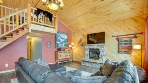 A cozy living room with a leather sofa, a stone fireplace, and a wooden staircase. - Spacious Gunnison Home: Ski, Hike, Bike & Fish! (Gunnison)