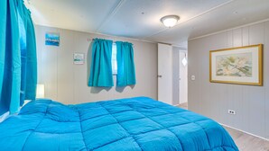 A bedroom with a large bed, teal curtains, a painting on the wall, and a door leading to another room. - 5 Mi to Golf: Charming Hernando Home w/ Deck (Hernando)