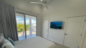 A bedroom with a large bed, a ceiling fan, a TV on the wall, and a view of the outdoors.