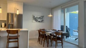 A modern kitchen with stainless steel appliances, a dining area with wooden chairs, and a large sliding glass door leading to an outdoor space.