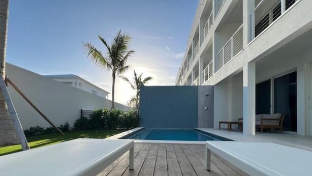 A modern pool area with a wooden deck, a clear blue pool, and a white building with balconies.