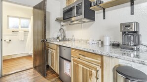 A compact kitchen with a stainless steel refrigerator, a microwave, a coffee maker, and wooden cabinets.