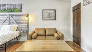 A room with a bed, a sofa, a wooden table, a map, and a door.
