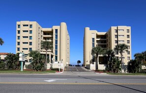 Stunning hotel building with a central vertical element, set amidst a beautifully landscaped garden with palm trees and shrubs.