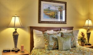Cozy retreat with a floral-patterned bedspread, framed landscape painting, and soft bedside lighting.
