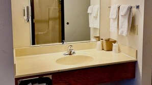 A bathroom with a sink, mirror, towel rack, and a laundry basket. - One queen bed, private bathroom with jetted tub, mini fridge, and single-serve coffee maker. (Boulder Junction)
